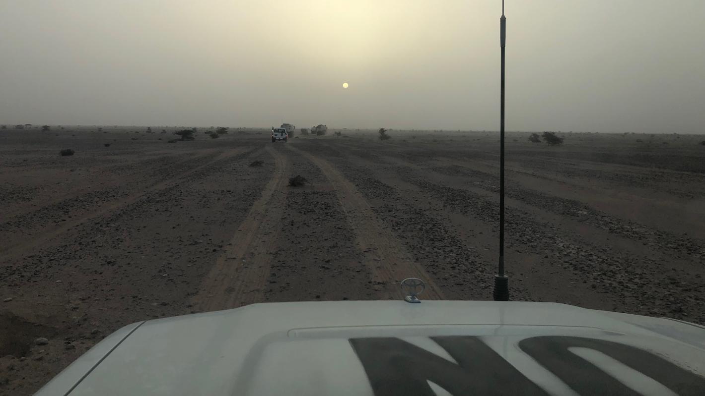 A vehicle marked UN drives along a desert road at sunset